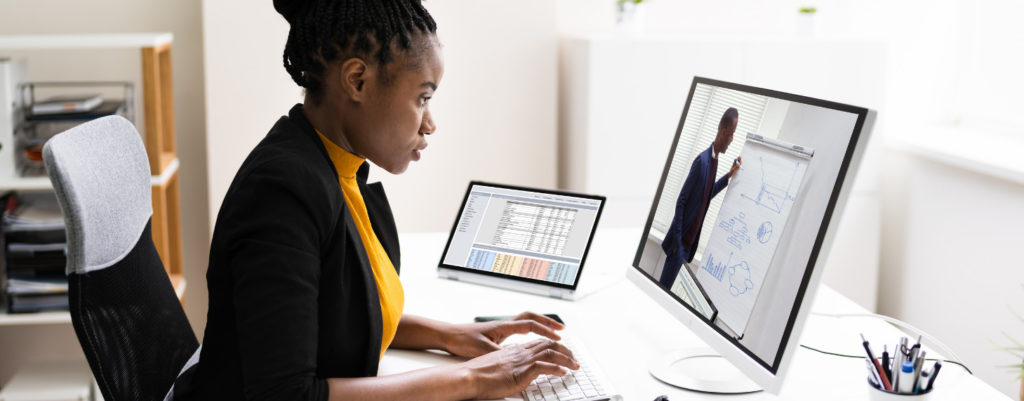 Woman sitting at a desk and typing as she watches a video of a man talking about different graphs and charts