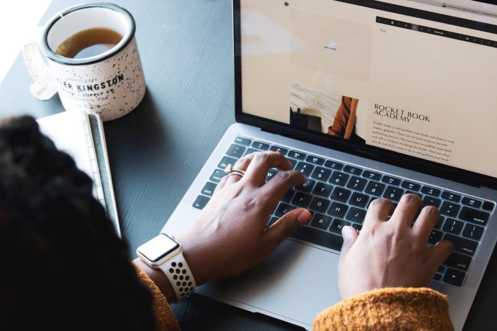 Person typing on a laptop computer, with cup of coffee next to their hands