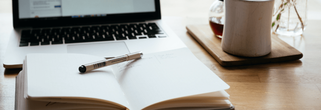 An open freelance copywriting journal sitting in front of a laptop